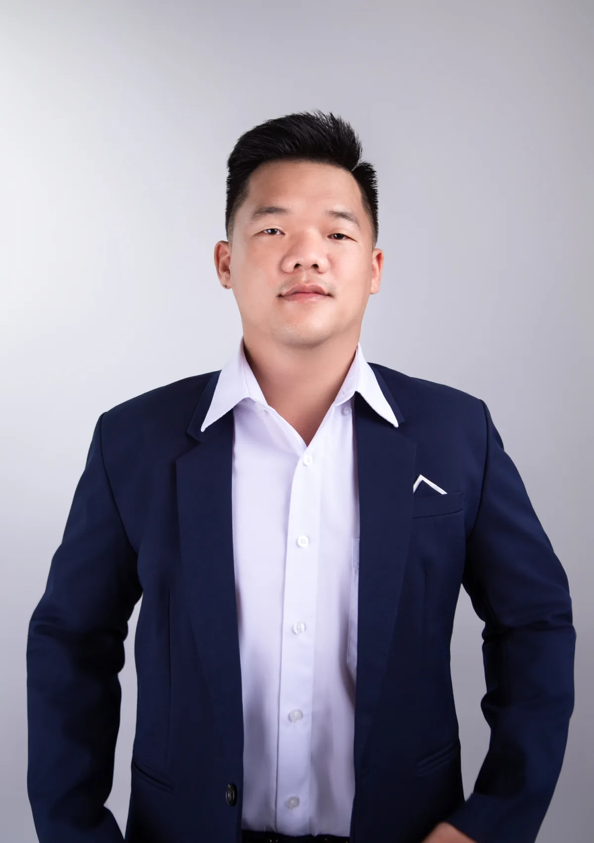 Le Pham in a navy jacket and open-collar white shirt, looking straight at the camera